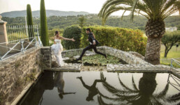 Marié sautant au-dessus d’un bassin pour rejoindre la mariée dans un jardin avec palmiers et paysage naturel.
