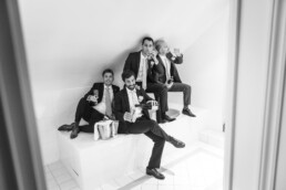 Quatre hommes en costume assis dans une salle carrelée, trinquant et buvant du champagne dans une ambiance festive.