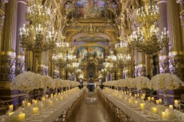 Grande salle richement décorée avec lustres dorés, longues tables dressées et compositions florales blanches pour un dîner de mariage.