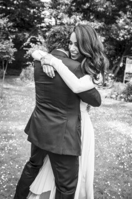 Mariés s’enlaçant dans un jardin, la mariée souriante pendant un moment d’émotion.