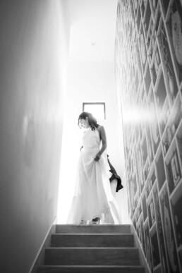 Mariée en robe fluide descendant un escalier lumineux, en noir et blanc, avant la cérémonie de mariage.