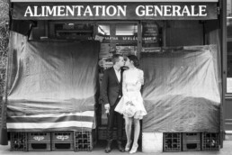 Couple de mariés s’embrassant devant une épicerie de quartier.