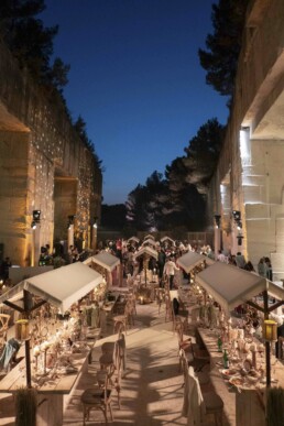 Tables de réception de mariage dressées en extérieur dans un lieu monumental éclairé au crépuscule.