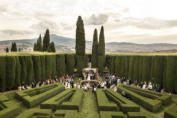 Cérémonie de mariage dans un jardin symétrique entouré de cyprès et de collines.