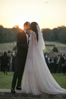 Mariés s’embrassant au coucher du soleil devant leurs invités.