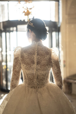 Mariée vue de dos portant une robe en dentelle dans un hall lumineux.