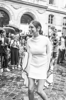 Mariée souriante tenant son bouquet devant les invités.