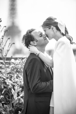 Une mariée et un marié s’embrassent tendrement en extérieur, avec une tour floue en arrière-plan.