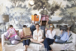 Une mariée assise sur un canapé entourée de ses amies qui tiennent des livres devant leur visage.