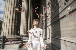 Mariée souriante sous des pétales de fleurs devant une église.