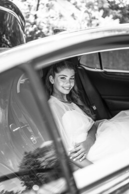 Mariée souriante assise à l’arrière d’une voiture de mariage.