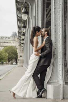 Les mariés s’offrent un moment de tendresse, à l’abri de la structure métallique du pont, dans une atmosphère intime et élégante.