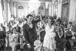 Les mariés lèvent les bras ensemble devant leurs invités qui applaudissent dans une salle de mariage élégante.