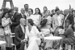 Les mariés s’embrassent devant leurs invités avec la tour Eiffel en arrière-plan.