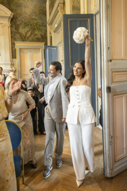 Les mariés sortent de la salle de cérémonie en levant les bras, acclamés par leurs proches.