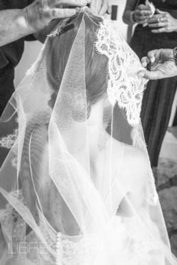 Des mains placent le voile en dentelle sur la tête de la mariée.