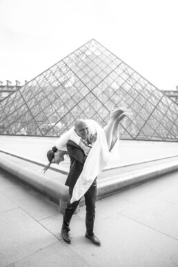 Un marié porte la mariée sur son épaule devant la pyramide du Louvre à Paris.