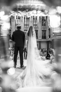 Mariés de dos sous une verrière fleurie face aux invités.