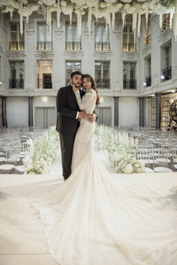 Mariés posant dans une allée fleurie sous une verrière.