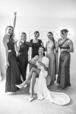 Mariée assise avec un verre entourée de demoiselles d’honneur qui rient.